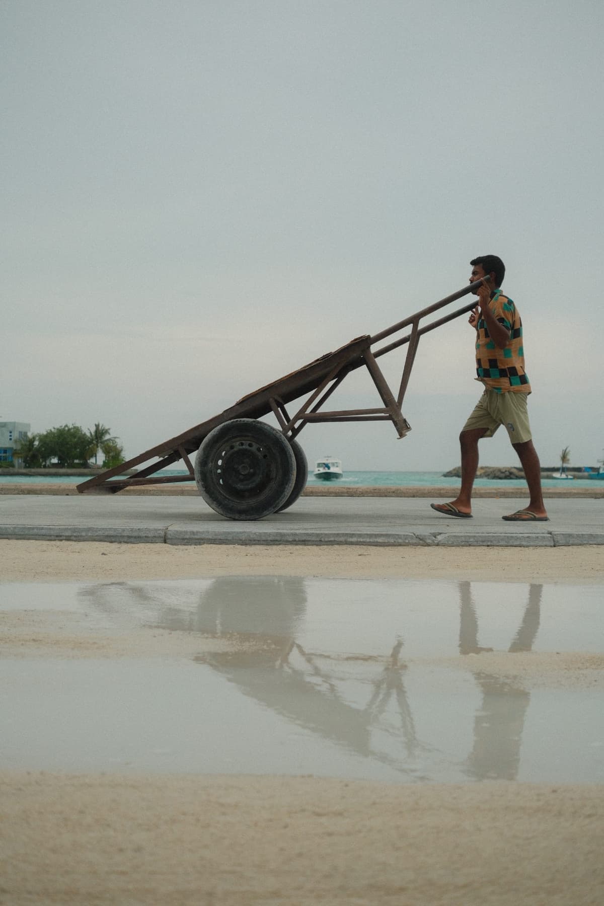 Man with cart reflected in a still harbor puddle