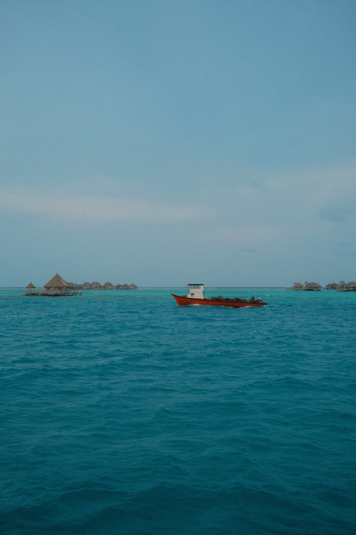 Red hull cutting across impossible blue, water huts distant