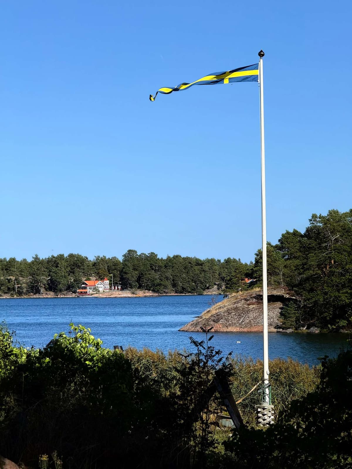 The Swedish flag out straight over the bay, houses on the far shore