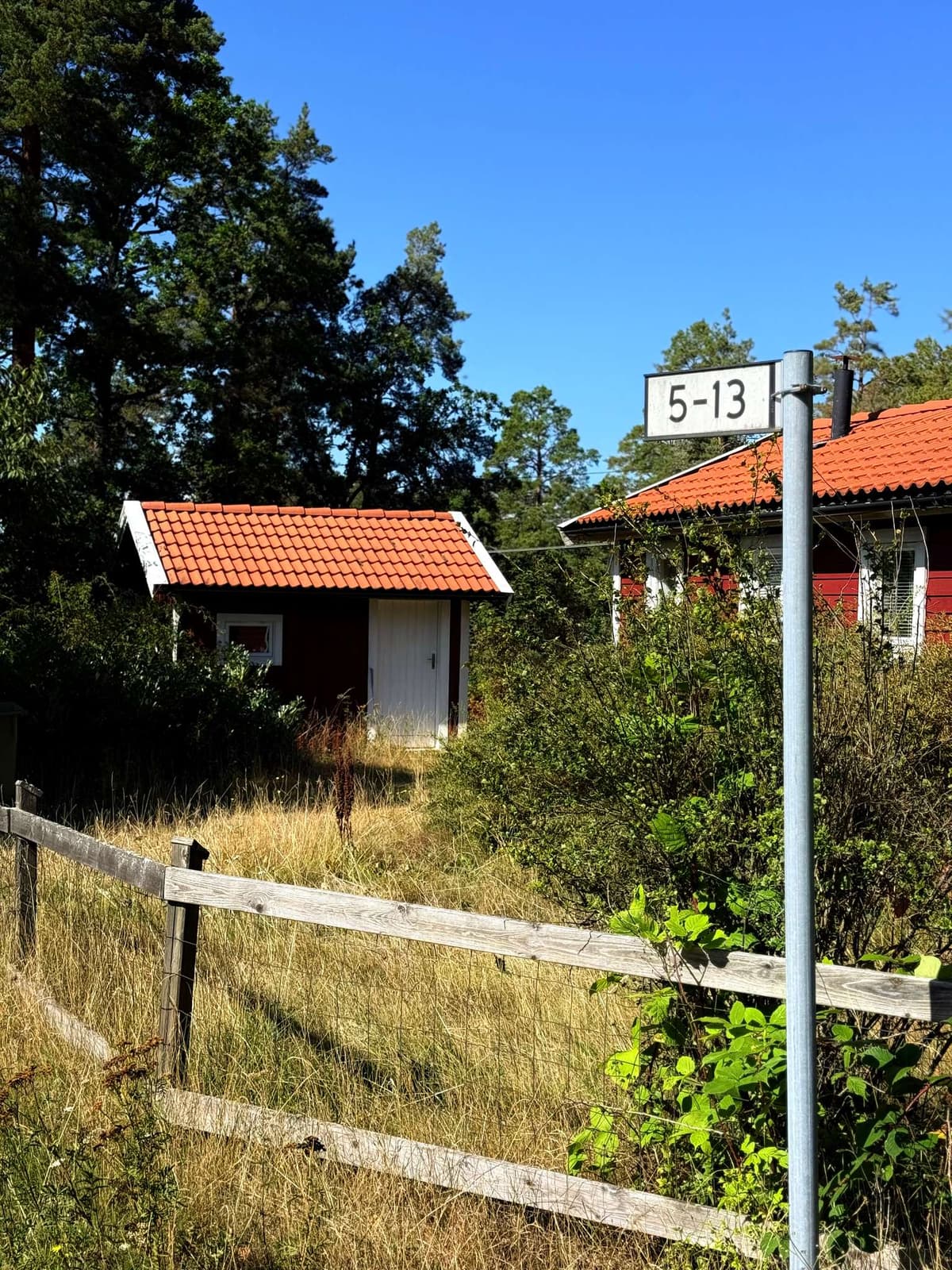 A small red cottage behind a wooden fence, the sign reading 5–13